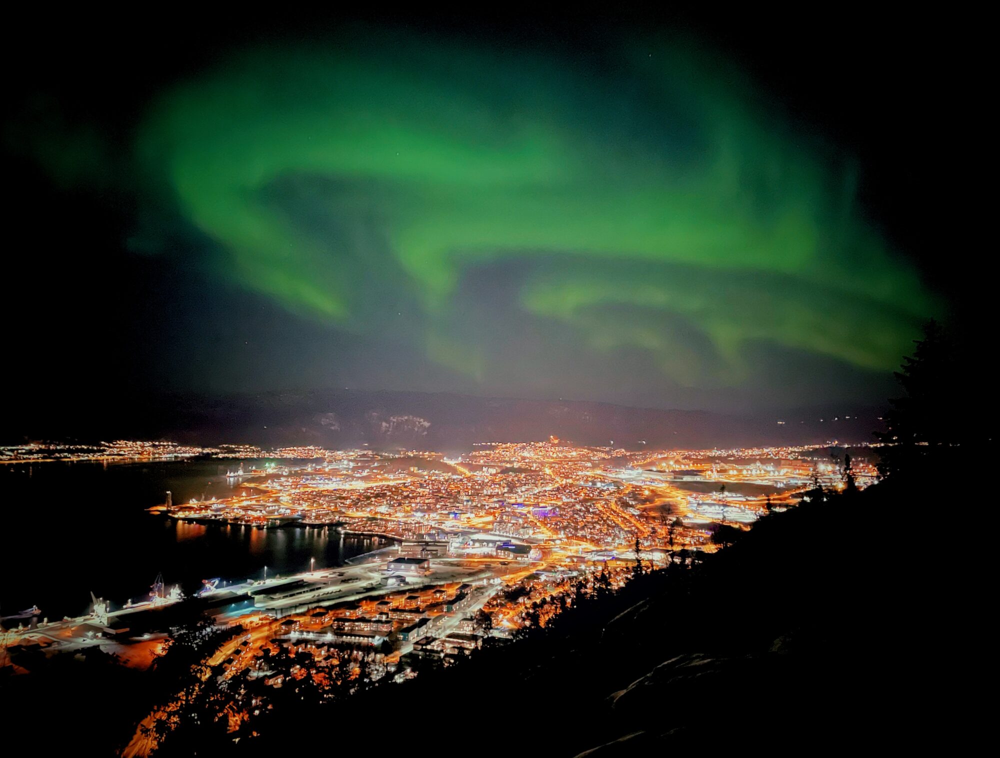 Grønt nordlys over en opplyst by i Nord-Norge