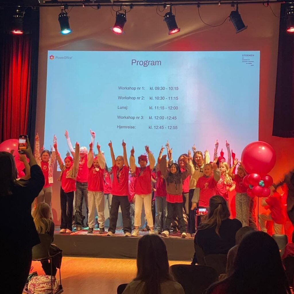 Deltakere på Girl Tech Fest står på scenen med hendene i været.